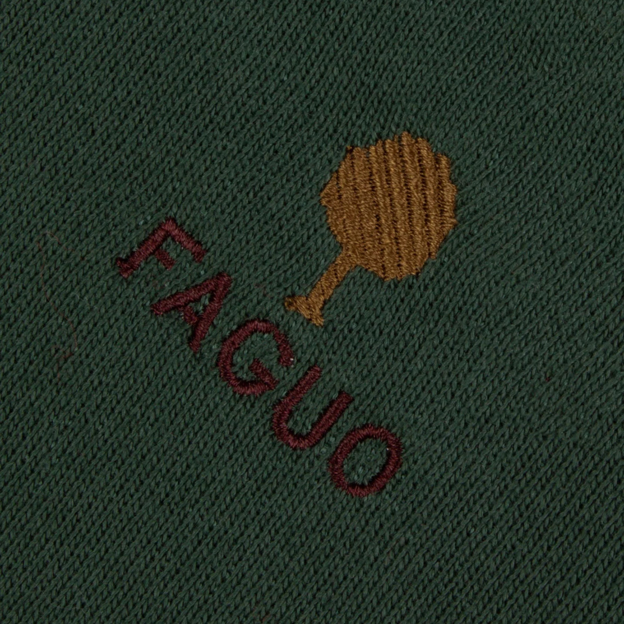 Gros plan de la broderie arbre ocre et du lettrage FAGUO bordeaux sur le molleton vert forêt