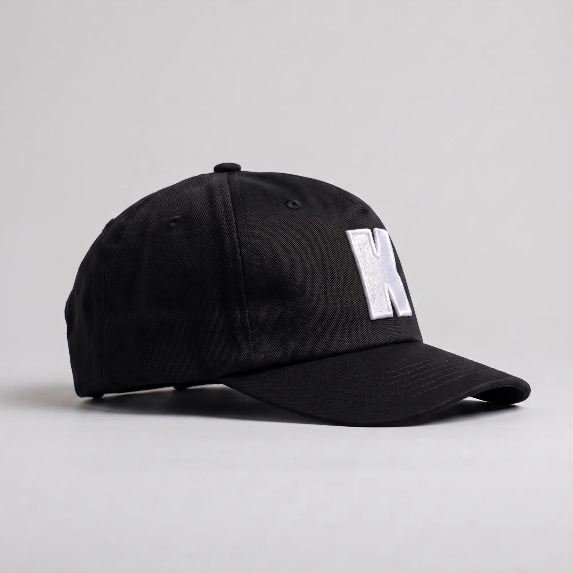 Profil droit de la casquette Klubb noire : calotte 5 panneaux sans renfort avant, visière incurvée, œillets brodés