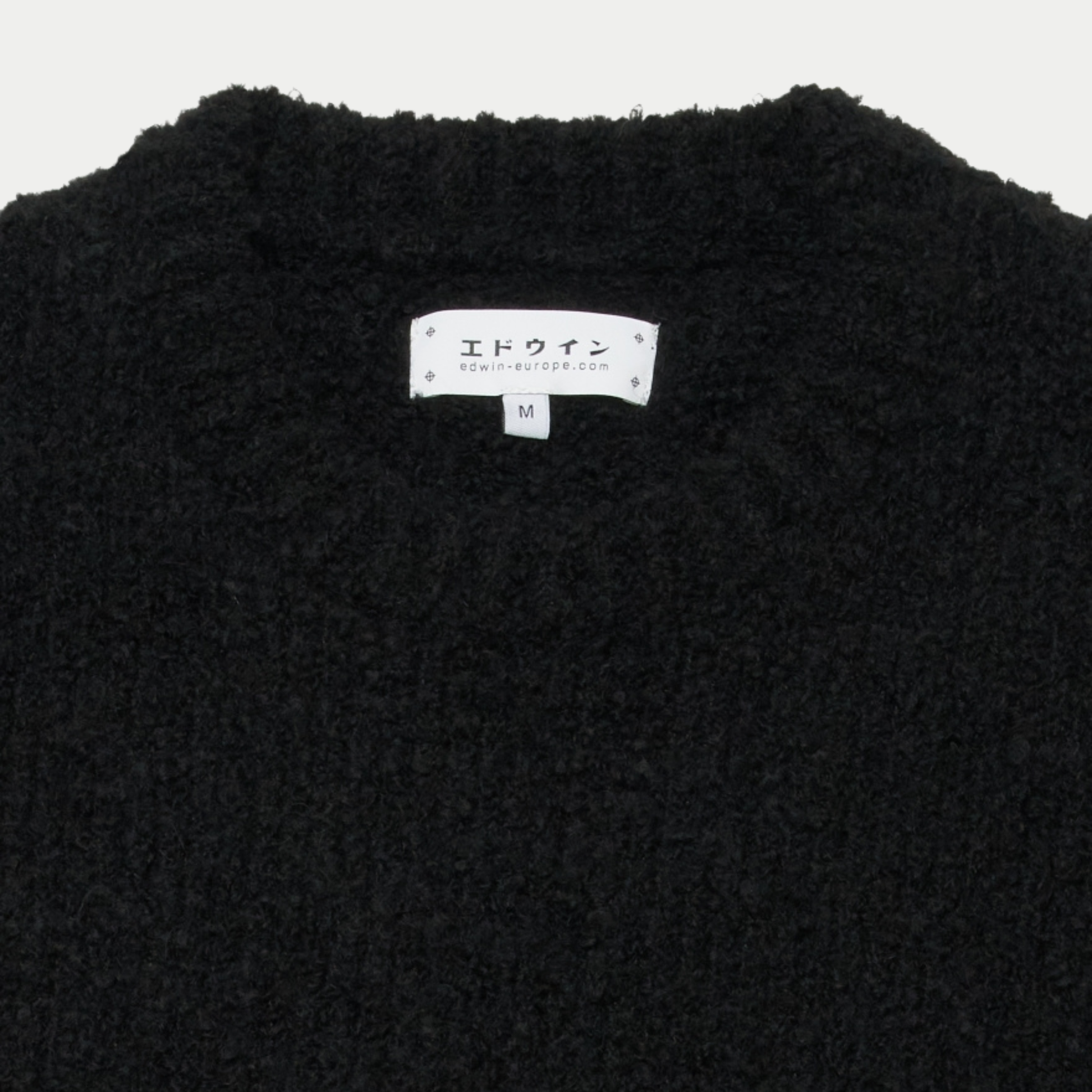 Détail du col rond du pull Dun Edwin noir et de son étiquette de marque intérieure