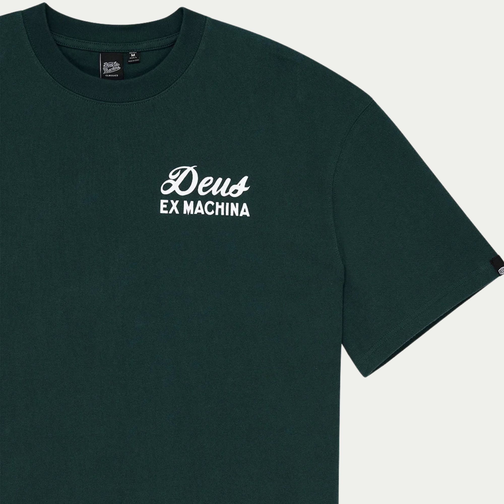 Gros plan du buste, logo Deus Ex Machina blanc et étiquette de col Classics sur le jersey vert sapin
