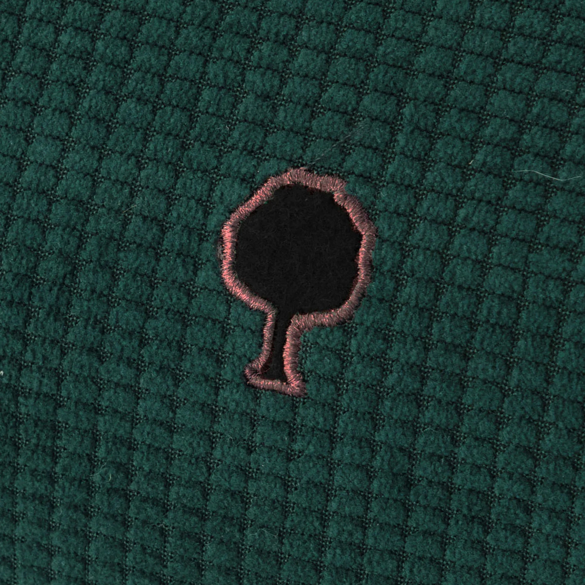 Gros plan sur le velours côtelé vert foncé de la trousse Faguo et son arbre brodé cerclé de rose
