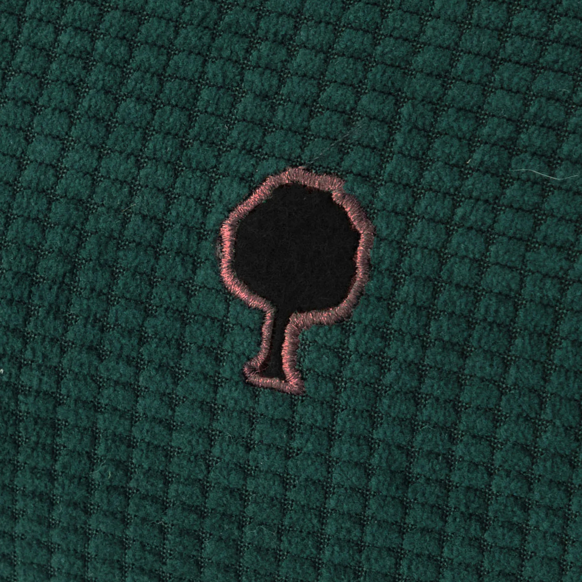 Gros plan sur le velours côtelé vert foncé de la trousse Faguo et son arbre brodé cerclé de rose