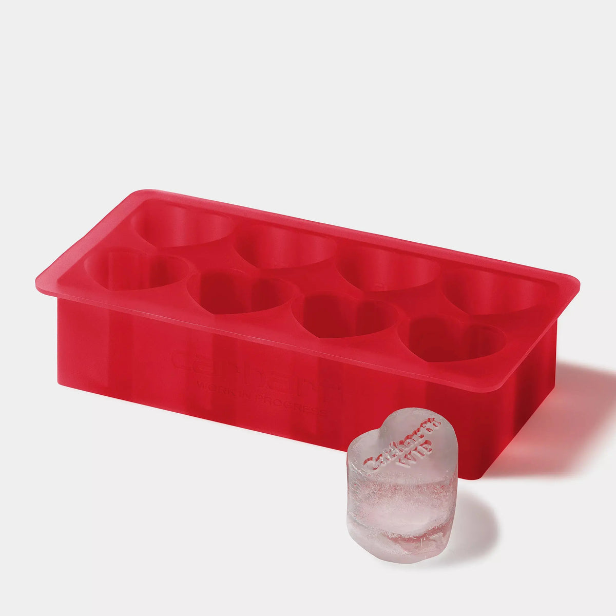 Bac à glaçons rouge en silicone, huit alvéoles en forme de cœur et glaçon cœur gravé posé juste devant