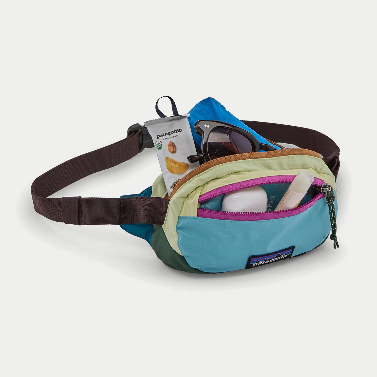 Banane Terravia Mini Hip Patagonia ouverte et garnie : lunettes, en-cas et coupe-vent, poche façade à zip magenta ouverte