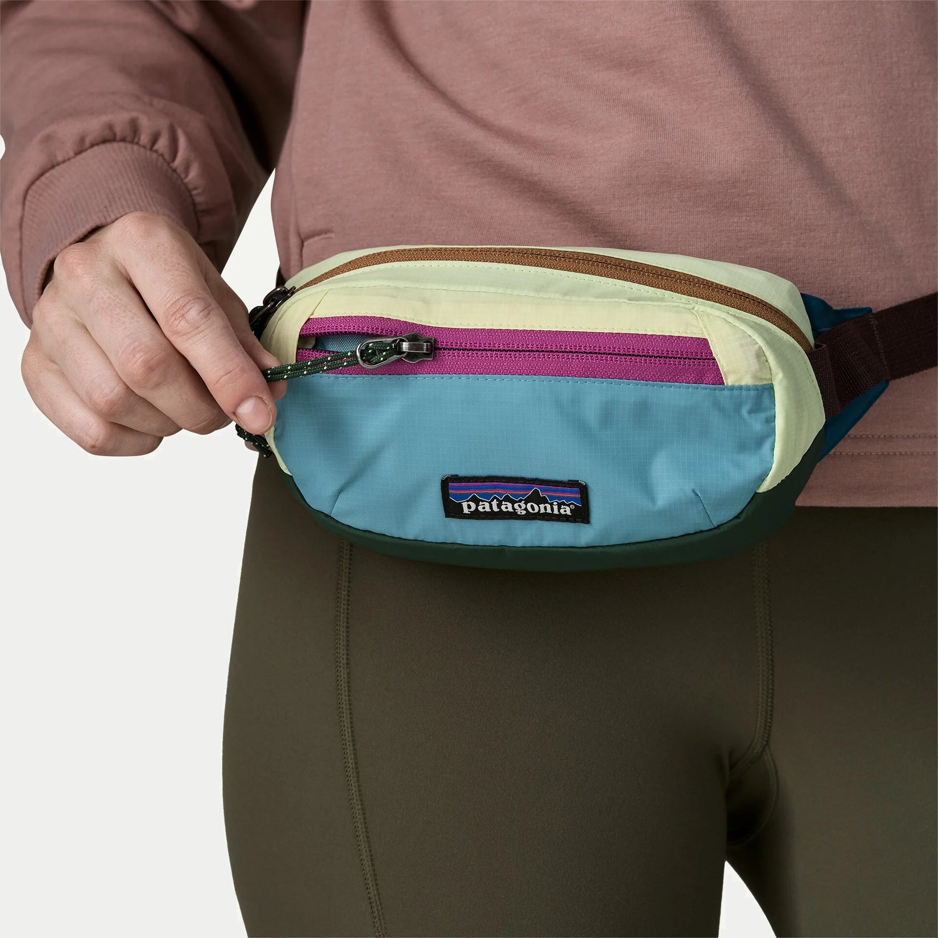 Gros plan sur la poche façade de la banane Terravia Mini Hip Patagonia : zip magenta ouvert, tirette cordelette verte