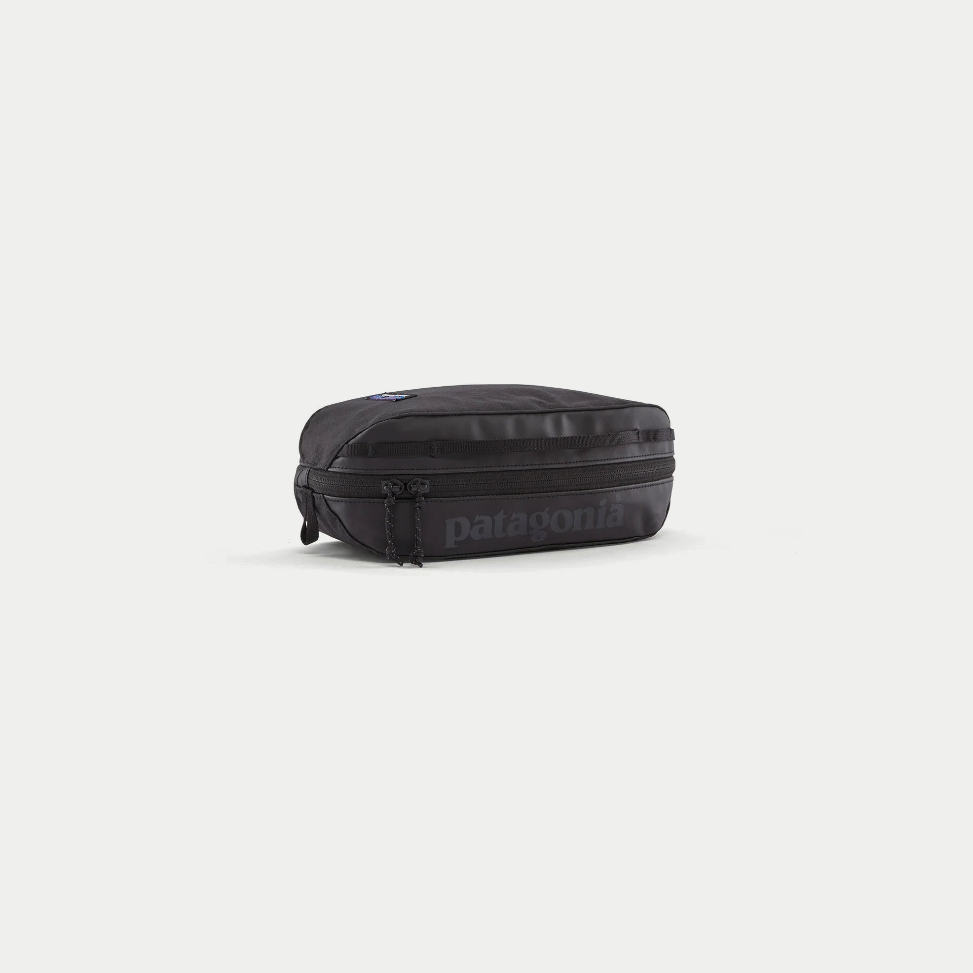 Cube Black Hole 3L noir Patagonia, trois quarts avant : logo ton sur ton, zip double curseur et sangle daisy chain