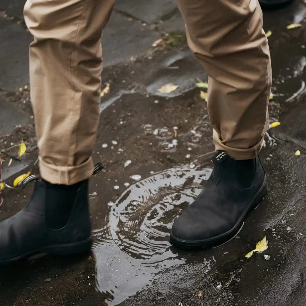 Boots Chelsea 587 anthracite portées sur un pavé mouillé avec un pantalon beige retroussé
