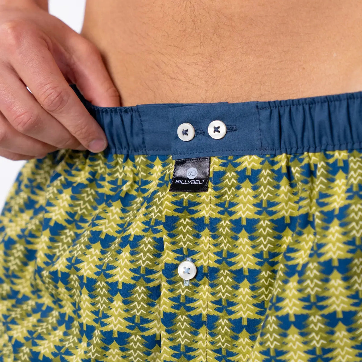 Ceinture bleu ardoise à deux boutons nacrés et étiquette BillyBelt noire sur l'imprimé forêt de sapins