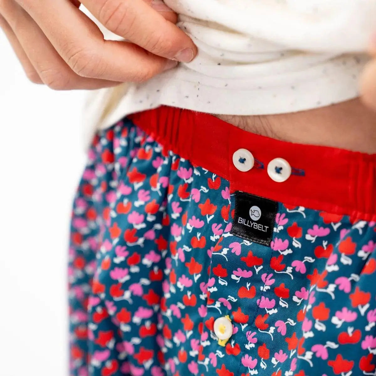 Gros plan sur la ceinture rouge, ses boutons nacrés et l'étiquette BillyBelt noire sur l'imprimé fleuri
