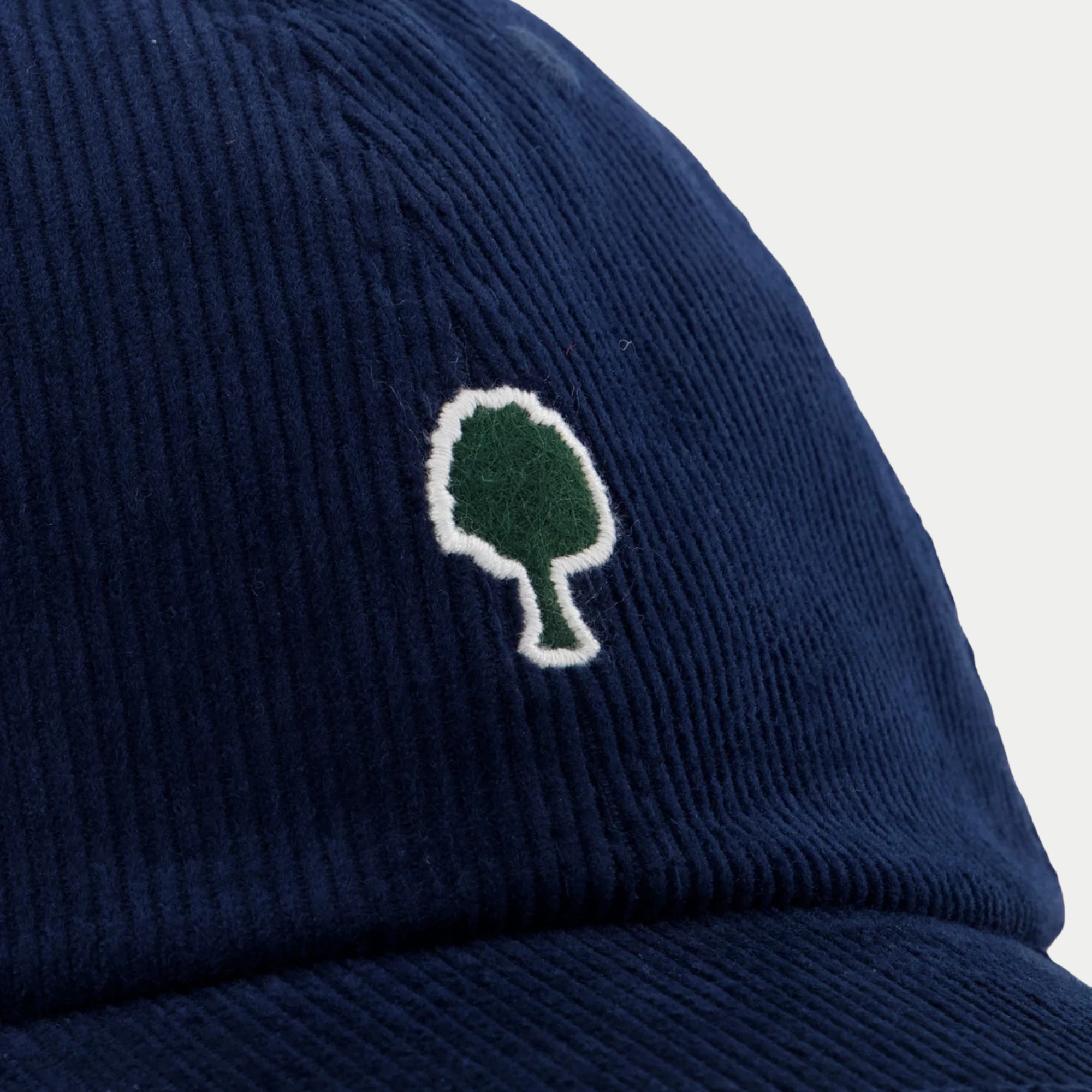 Détail macro des côtes du velours bleu foncé et de la broderie arbre vert bordée de blanc cassé, casquette Faguo