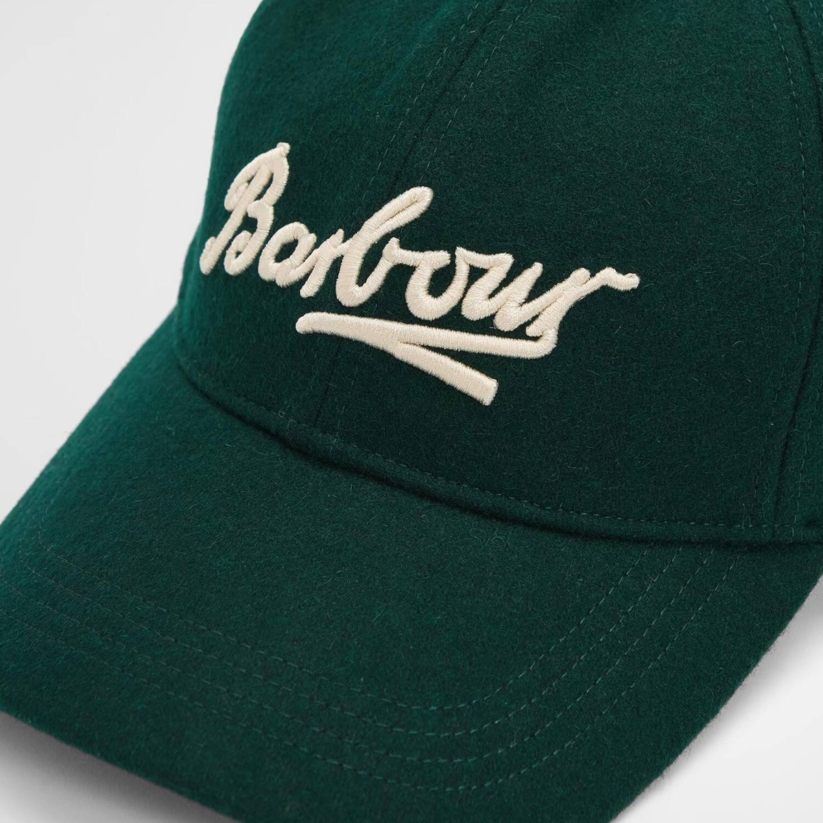 Gros plan du logo Barbour brodé écru en relief sur le drap de laine vert forêt de la casquette Bowery, visière surpiquée