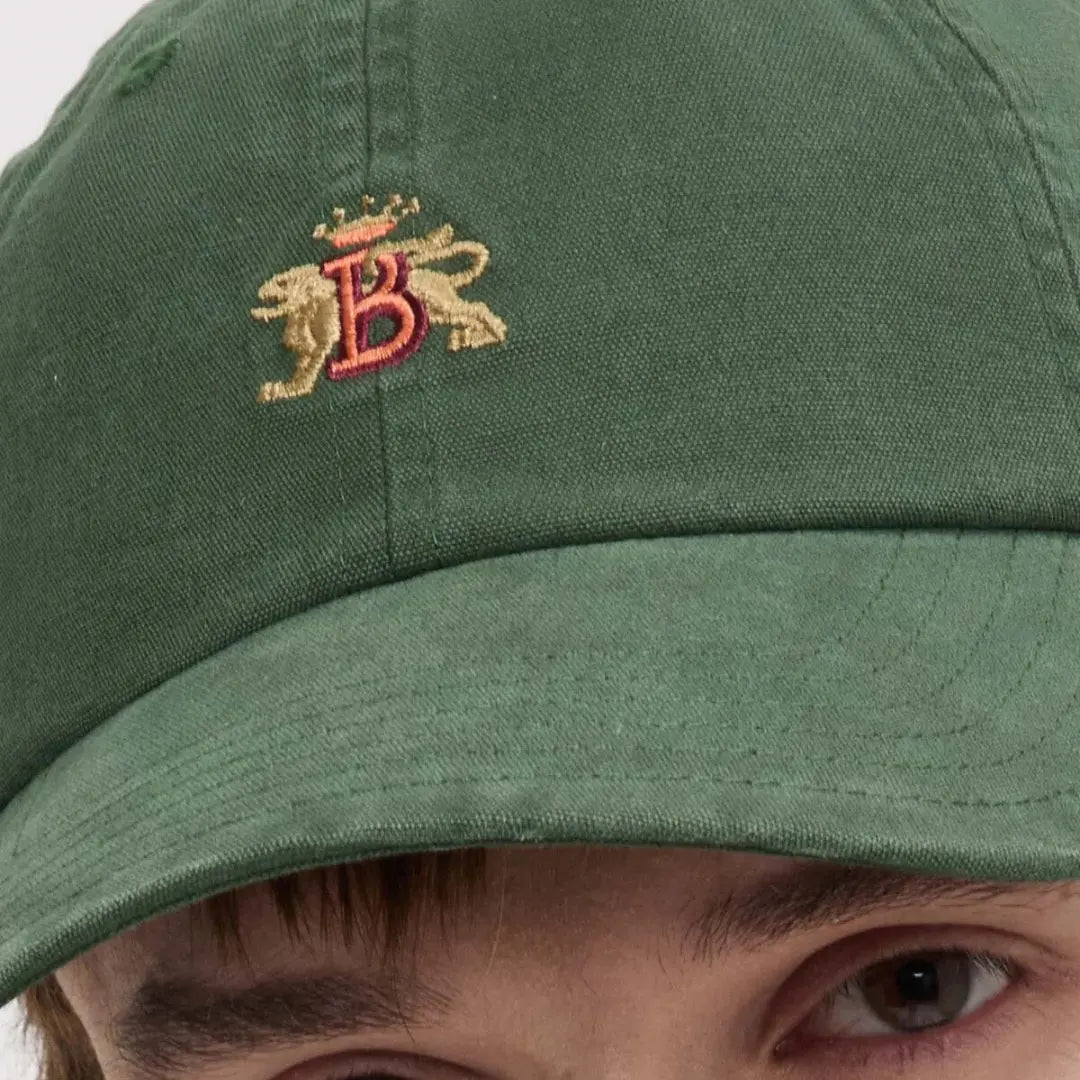 Macro portée : blason brodé or et rouge et visière surpiquée sur le coton vert sapin