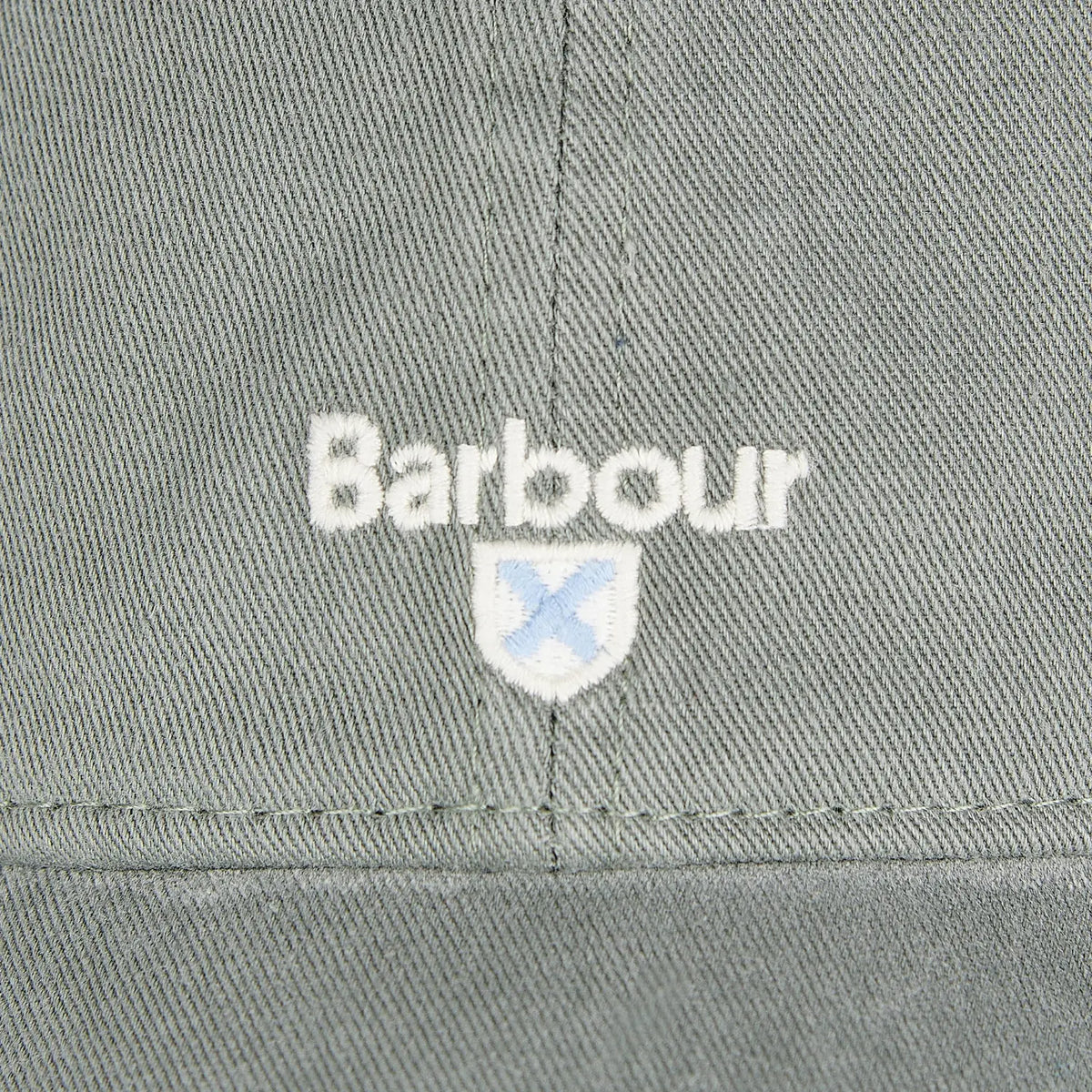 Macro du logo brodé écru et de l'écusson à croix bleu ciel sur twill vert gris