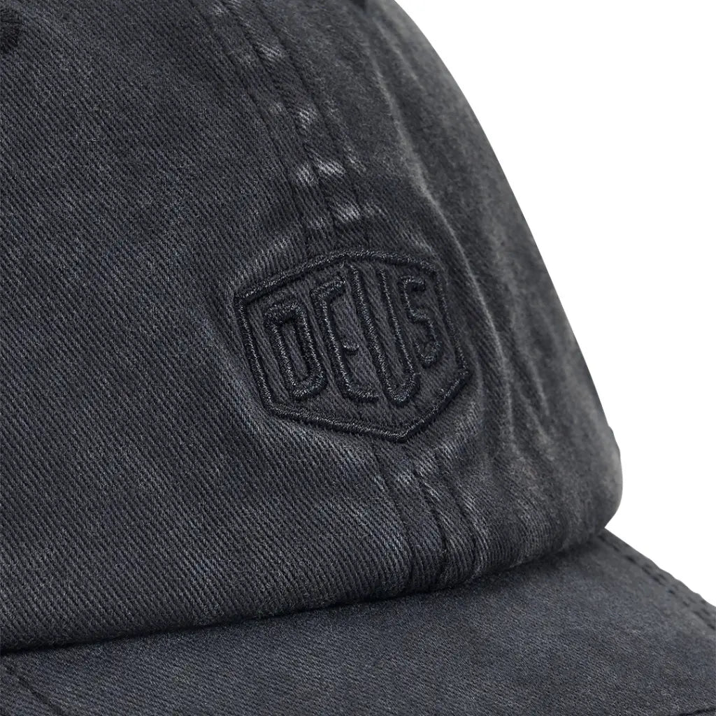 Gros plan du bouclier brodé noir sur la calotte noire délavée de la casquette Garment Dyed