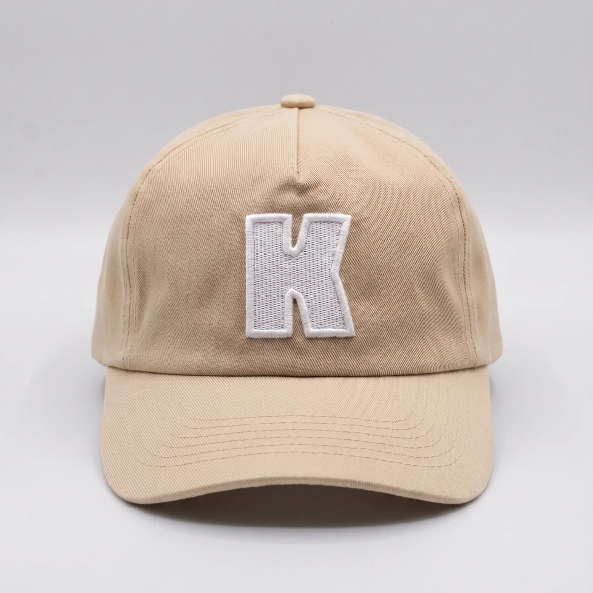 Casquette Klubb beige sable de face : K blanc brodé en relief, couture centrale de calotte et visière surpiquée