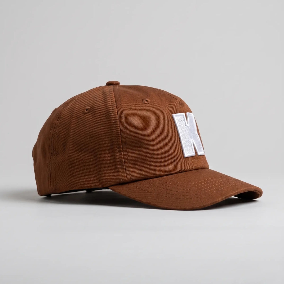 Casquette Klubb marron de profil : calotte souple, visière préformée surpiquée et œillets d’aération brodés