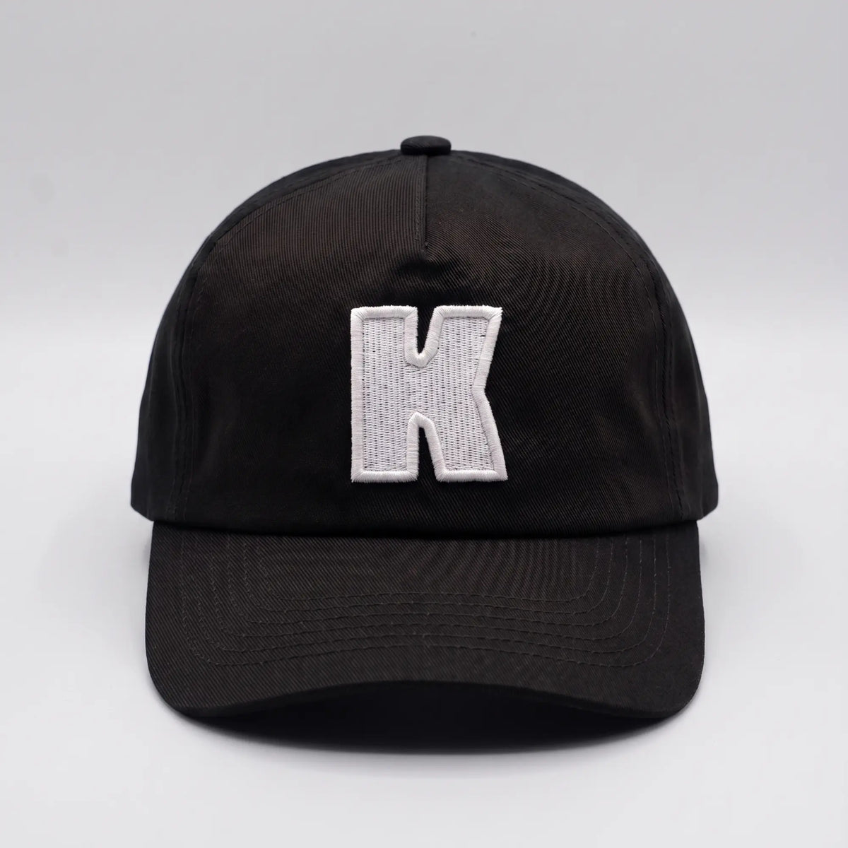 Vue de face de la casquette Klubb noire : K blanc brodé se détachant en fort contraste sur le sergé de coton noir