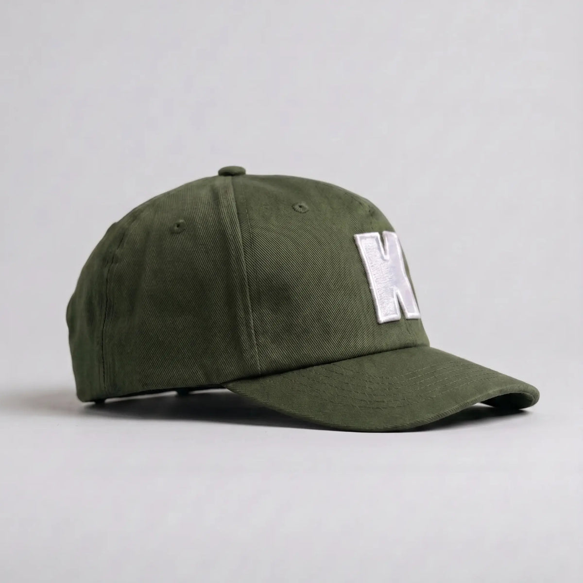 Casquette Klubb vert olive de trois-quarts : couronne basse et souple, aérations brodées et visière longue surpiquée