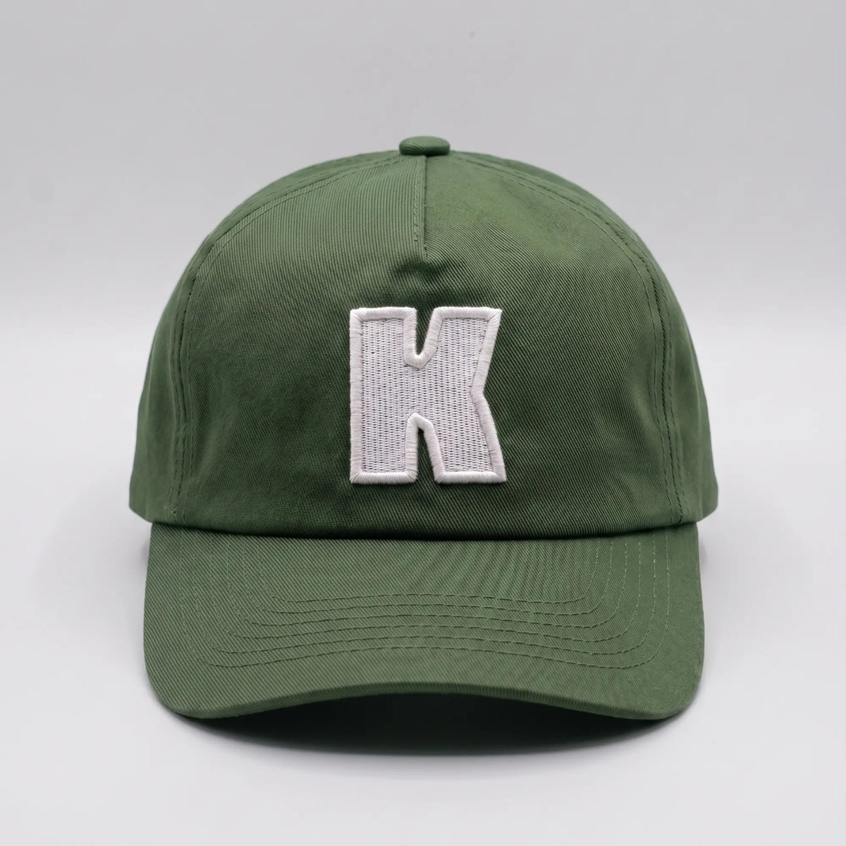 Casquette baseball Klubb vert olive grisé vue de face, grand K blanc brodé au centre du panneau avant et visière courbée