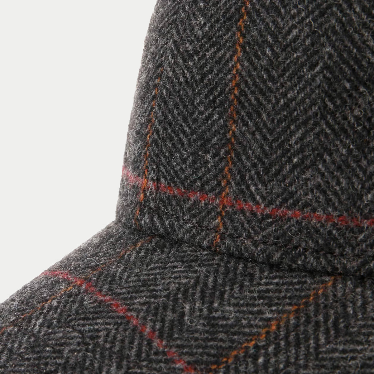 Gros plan sur la laine à chevrons gris anthracite et le carreau rouge et orange de la casquette Kinty
