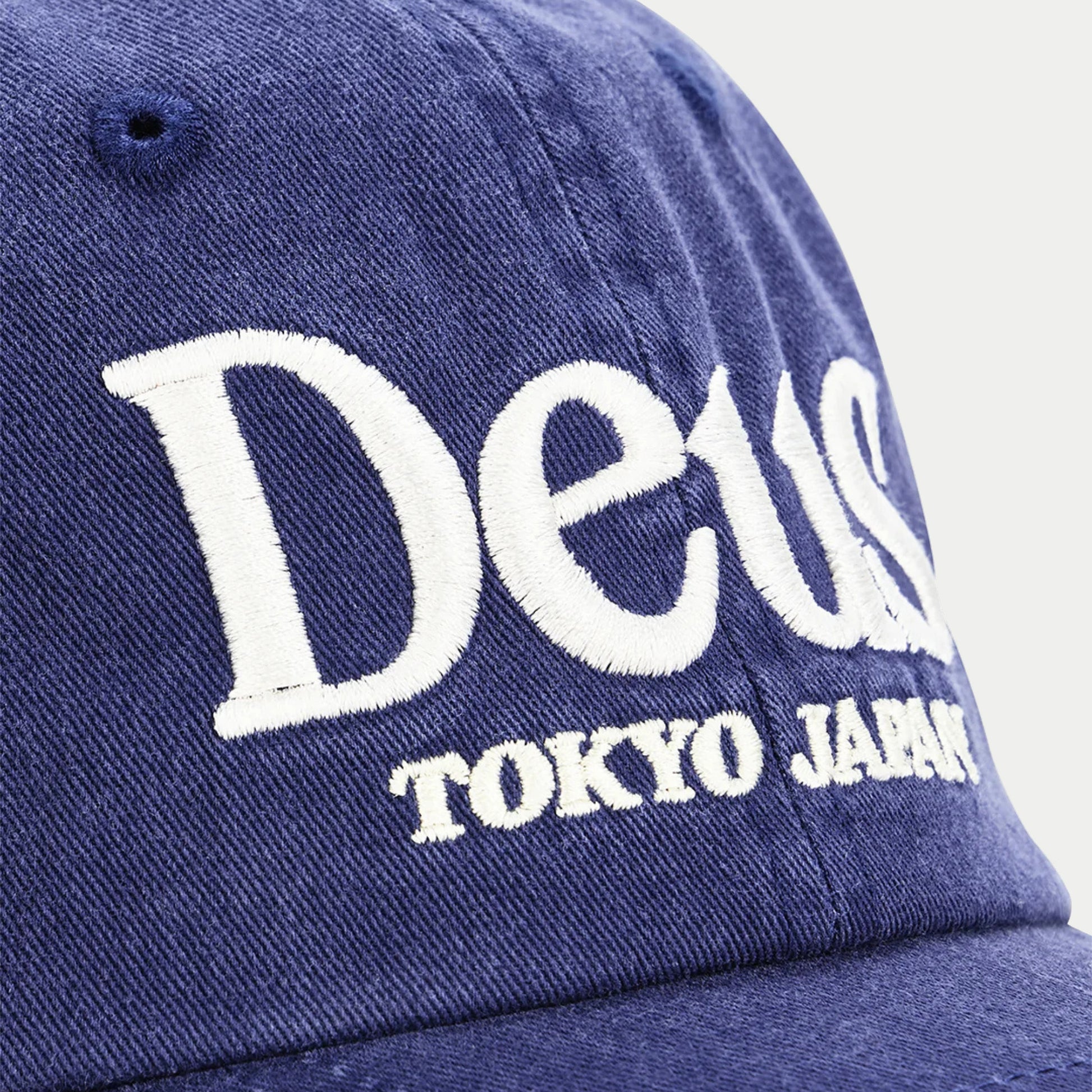 Macro de la broderie blanche haute densité de la casquette Metro indigo : lettrage sérif Deus en relief sur le sergé délavé