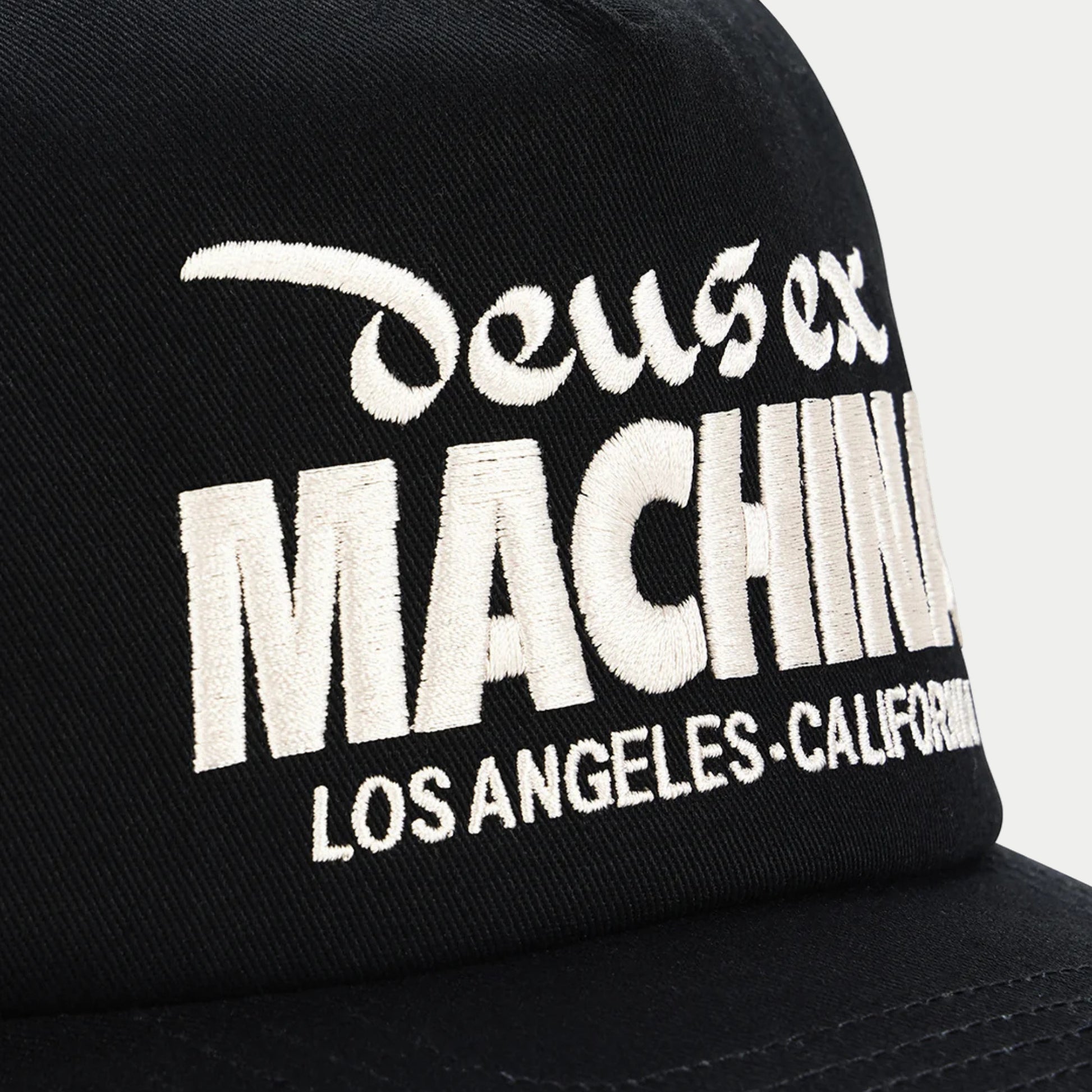 Broderie écrue MACHINA en gros plan sur le sergé noir de la casquette Primo Deus Ex Machina, armure diagonale visible