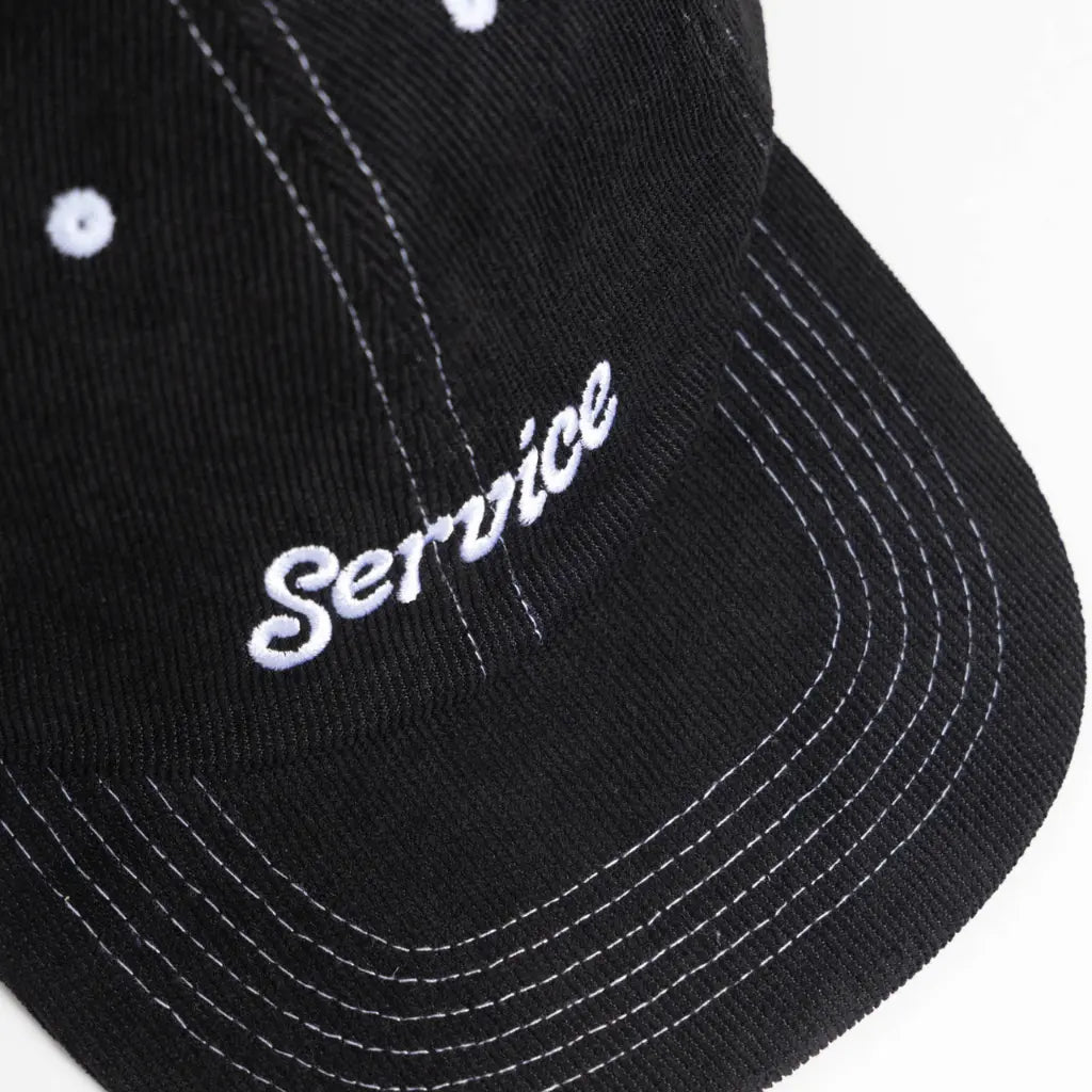 Gros plan du script blanc Service et des surpiqûres blanches en arcs sur la visière noire