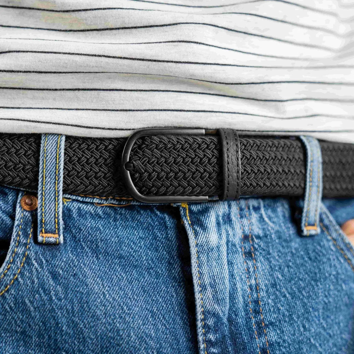 Tresse noire unie All Black bouclée à la taille d'un jean bleu clair, boucle noire mate sous un haut rayé écru
