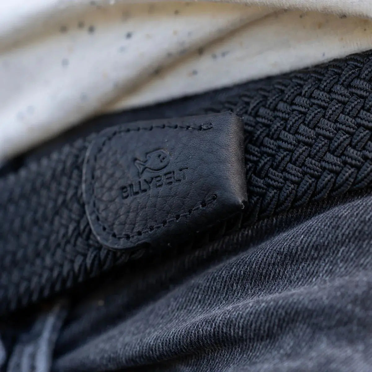 Patte de cuir noir grainé au poisson estampé, en bout de tressage noir All Black, sur un jean délavé sombre