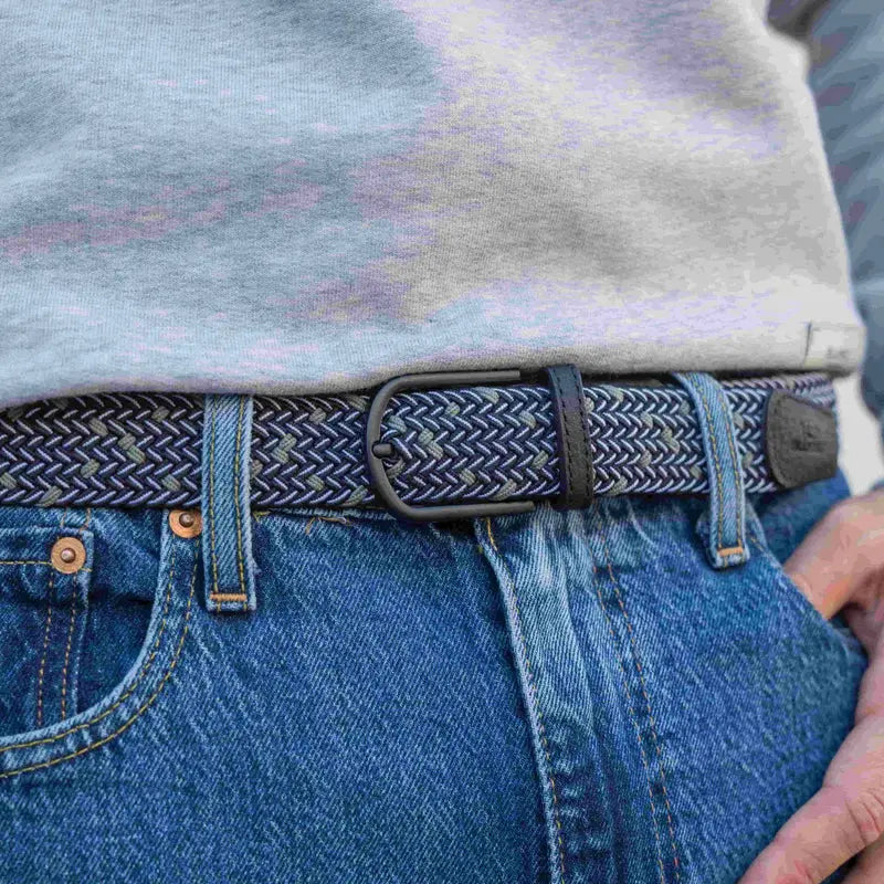 Ceinture tressée noire, blanche et gris-vert portée à la taille sur un jean bleu, sous un sweat gris chiné.