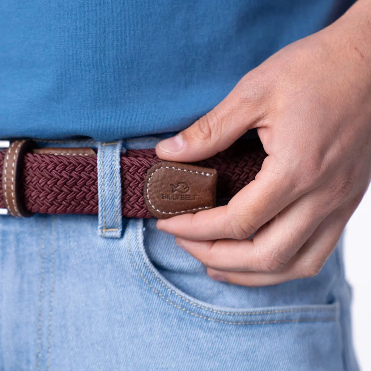 Embout en cuir grainé marron estampé BillyBelt au bout du tressage bordeaux du modèle Lie de Vin, sur un jean clair