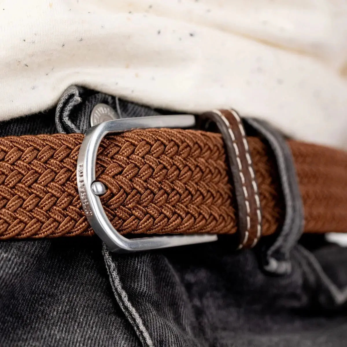 Macro de la boucle argentée refermée sur le tressage fauve caramel, chaque fil de la natte nettement détaché