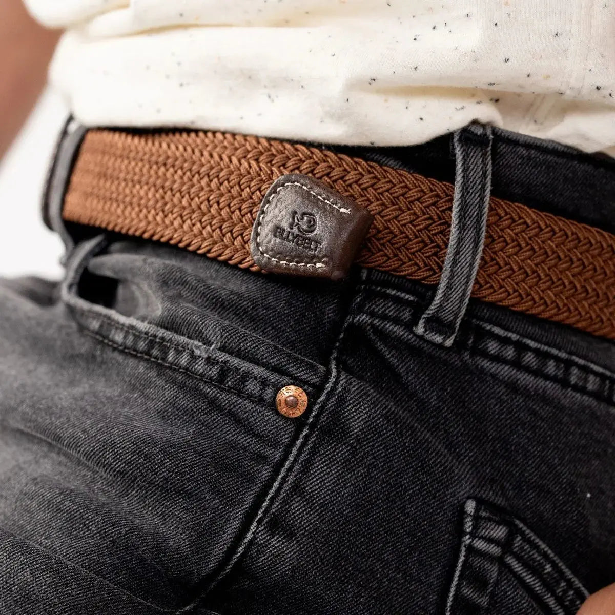 Embout carré en cuir marron foncé estampé BillyBelt au bout du tressage caramel, porté sur un jean noir
