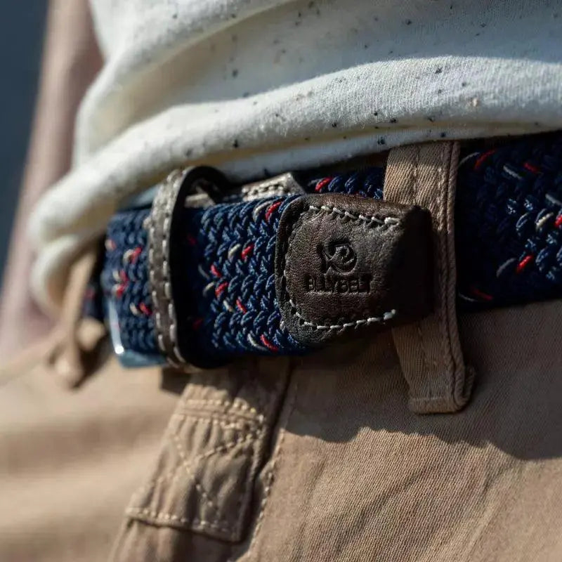 Ceinture Oxford bleu marine mouchetée de rouge et de blanc portée sur un chino beige, embout de cuir marron estampé