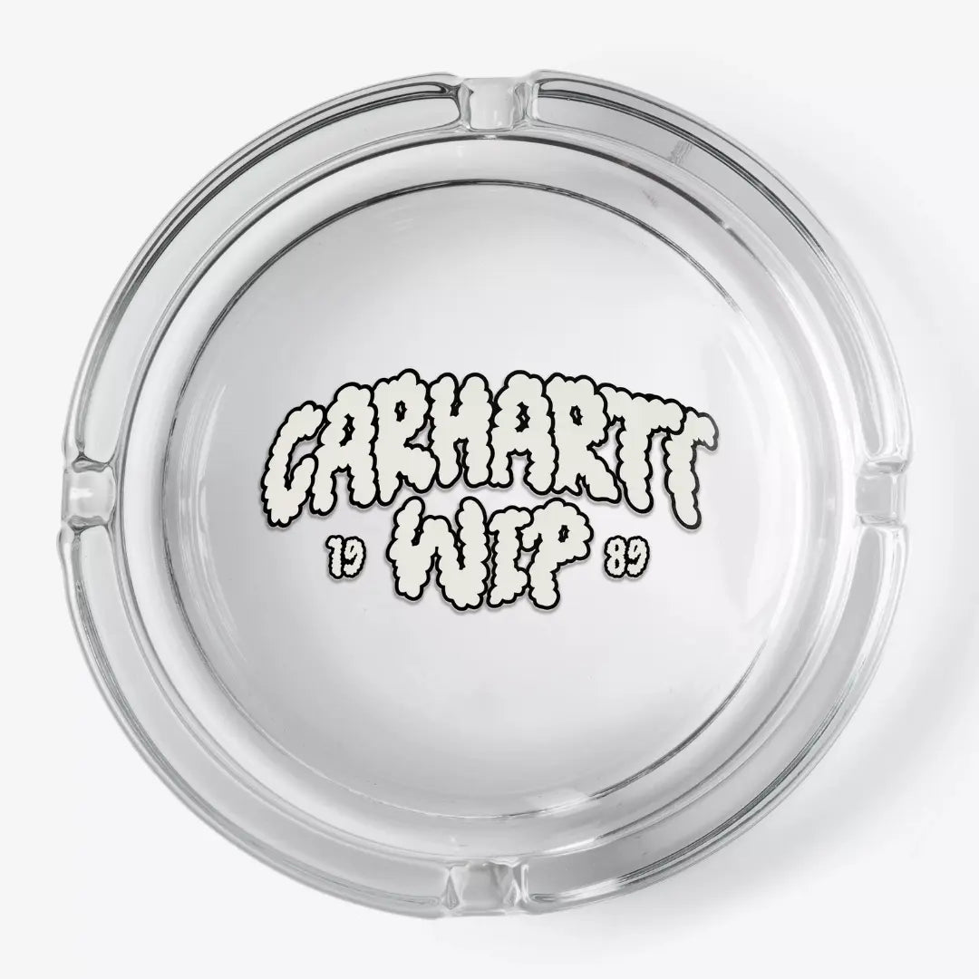 Cendrier rond en verre transparent vu de dessus, lettrage nuage crème 1989 au fond et quatre encoches