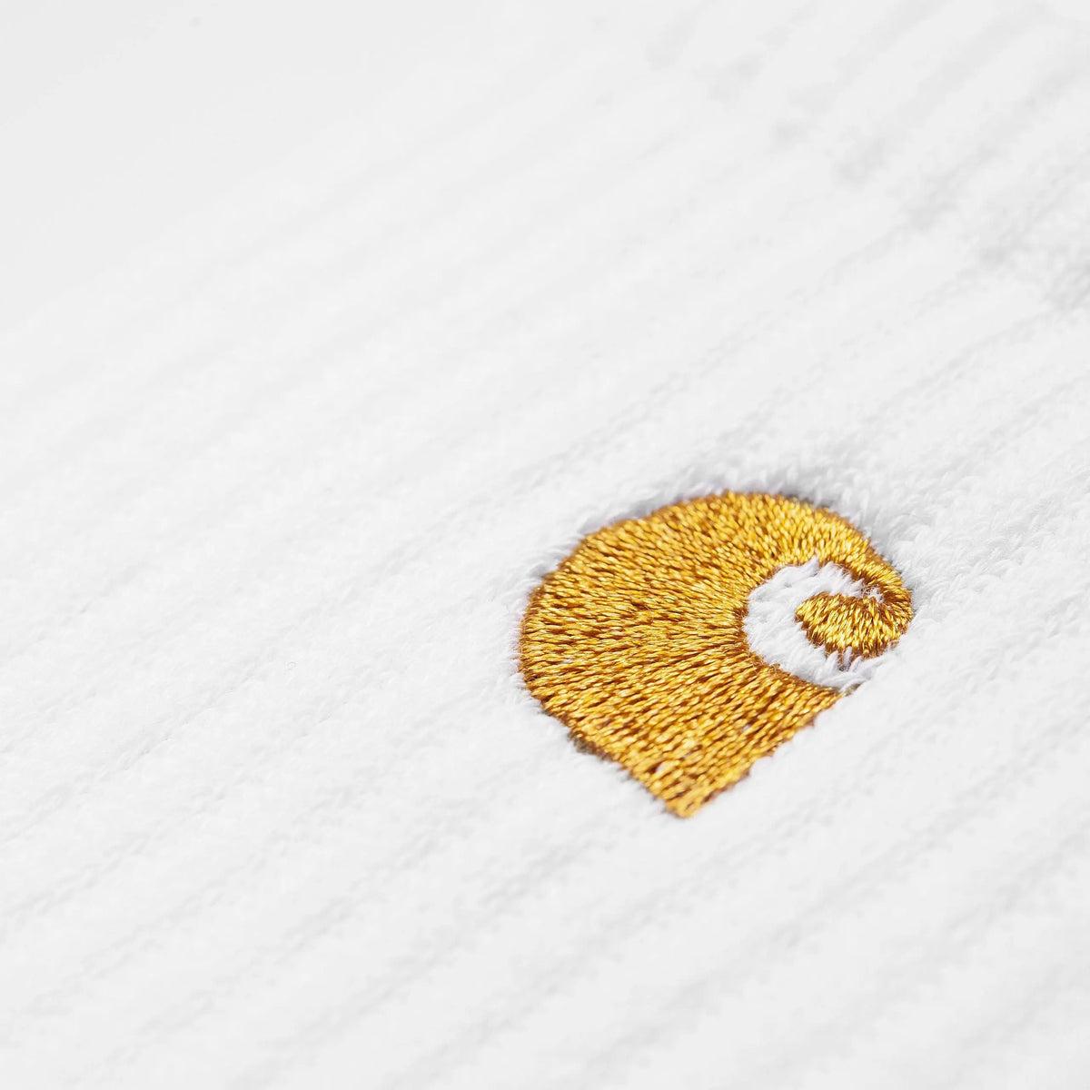 Macro du logo C brodé en fil doré satiné, posé sur la maille blanche finement côtelée d'une chaussette Chase