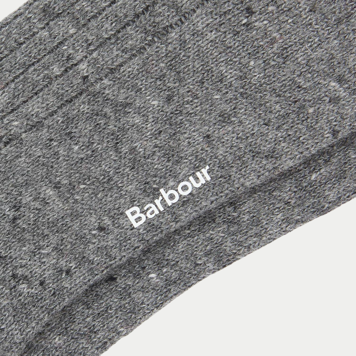 Détail macro de la maille gris chiné piquée de neps blancs, logo Barbour blanc sur le côté de la tige.