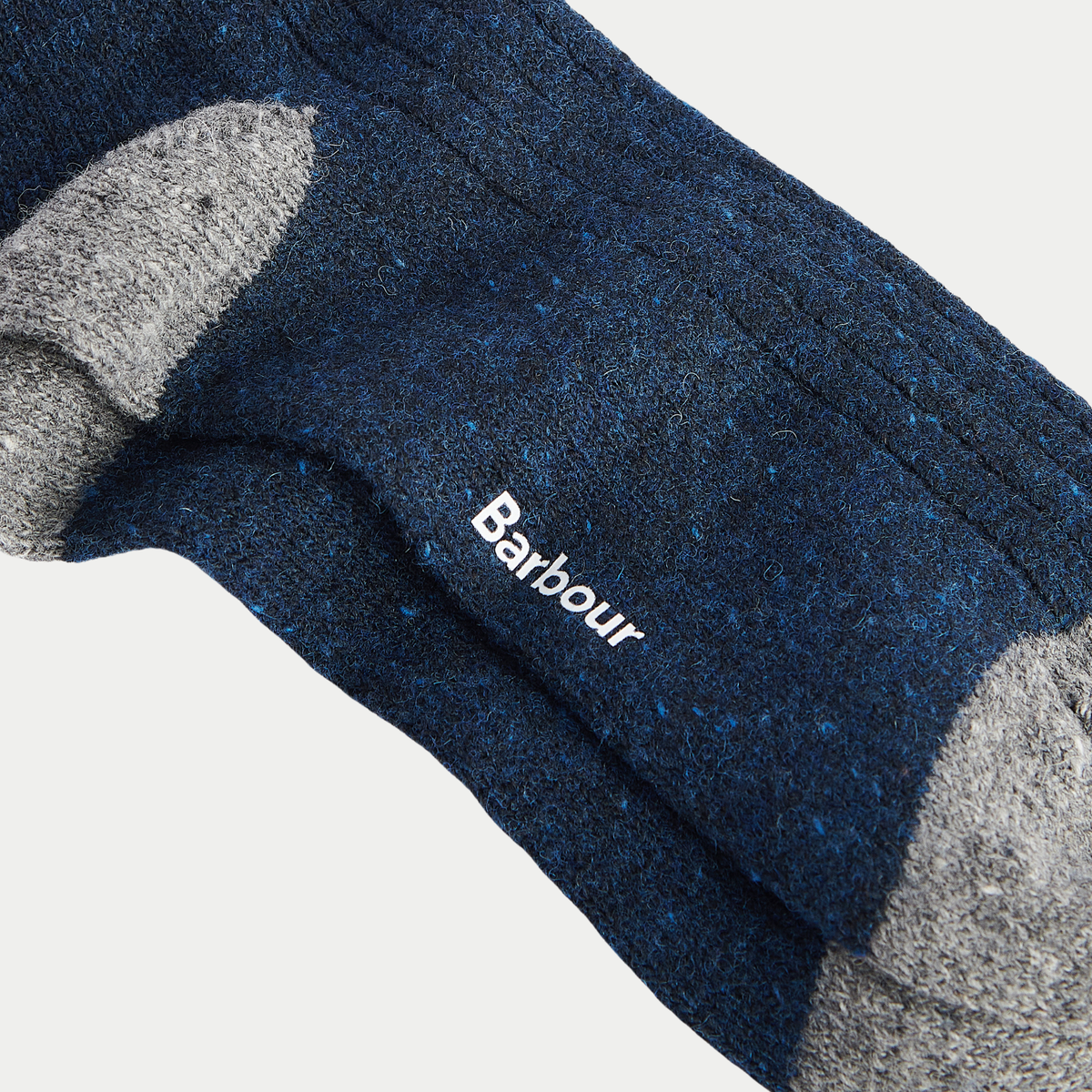 Zoom sur la laine Midnight aux neps bleu vif, logo Barbour blanc et pointe gris chiné en arrière-plan.