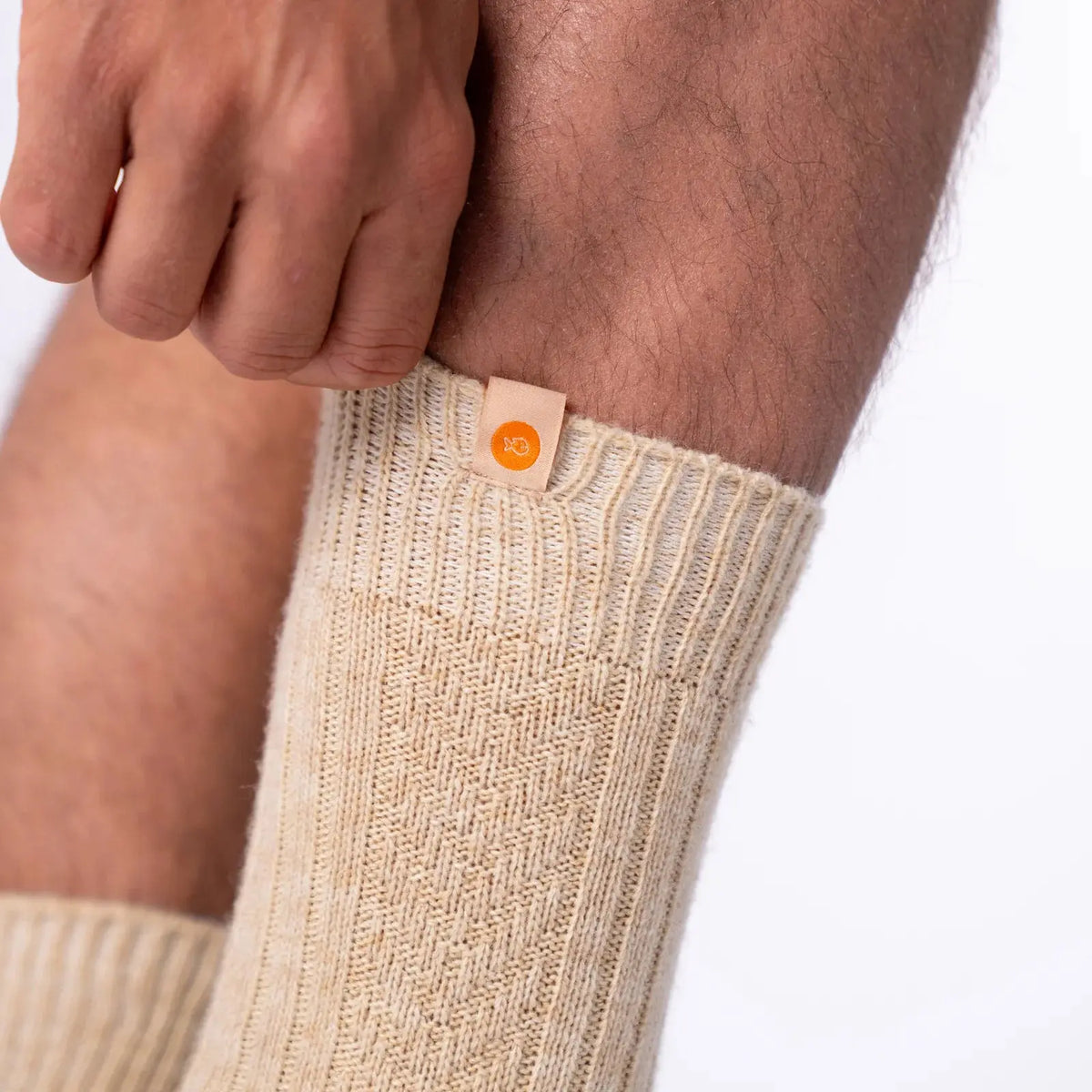 Macro de la laine écrue : côtes en relief, damier tricoté et petite étiquette beige à pastille orange