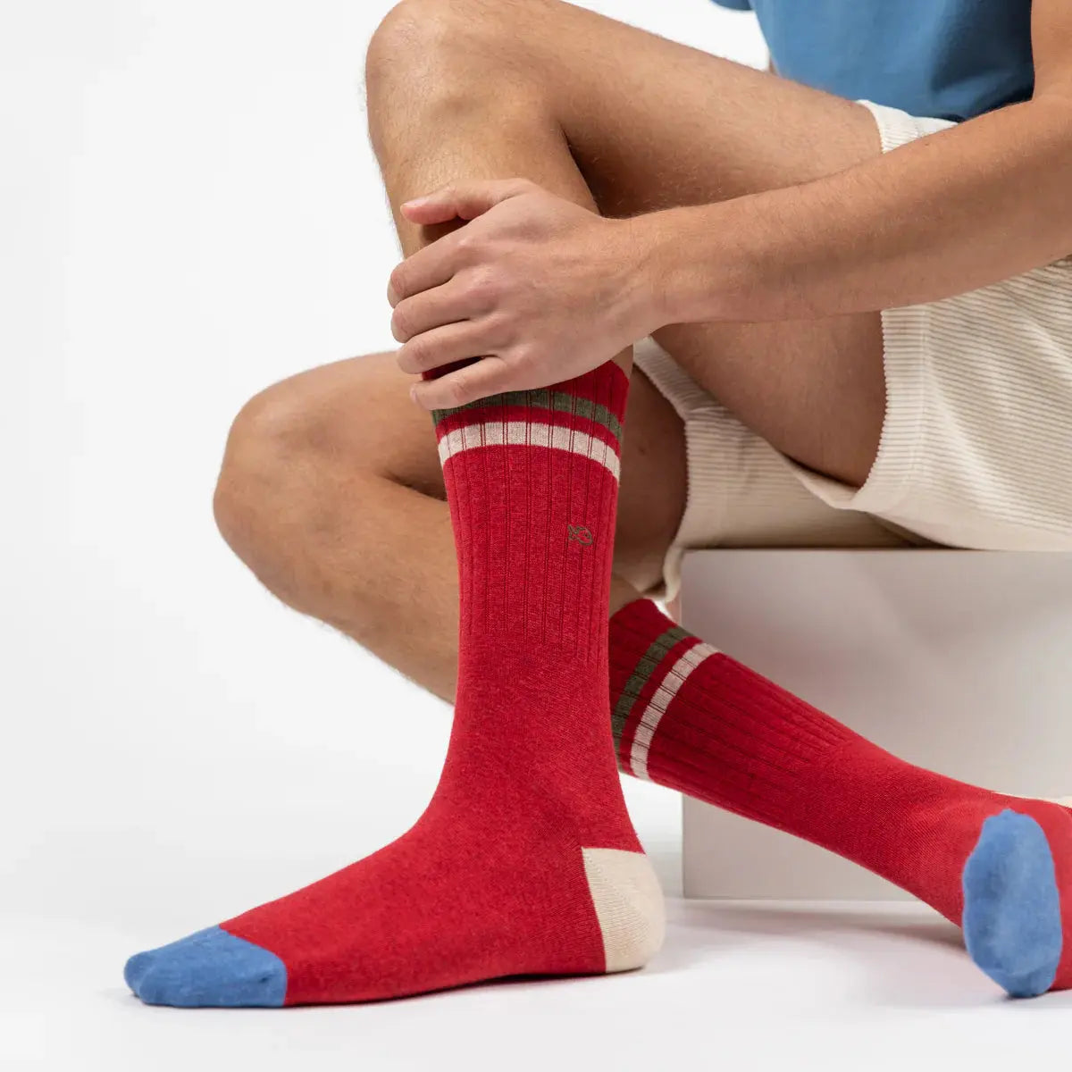 Paire rouge côtelée portée assise, bandes kaki et écrue en haut de tige, talon écru et pointes bleu jean.