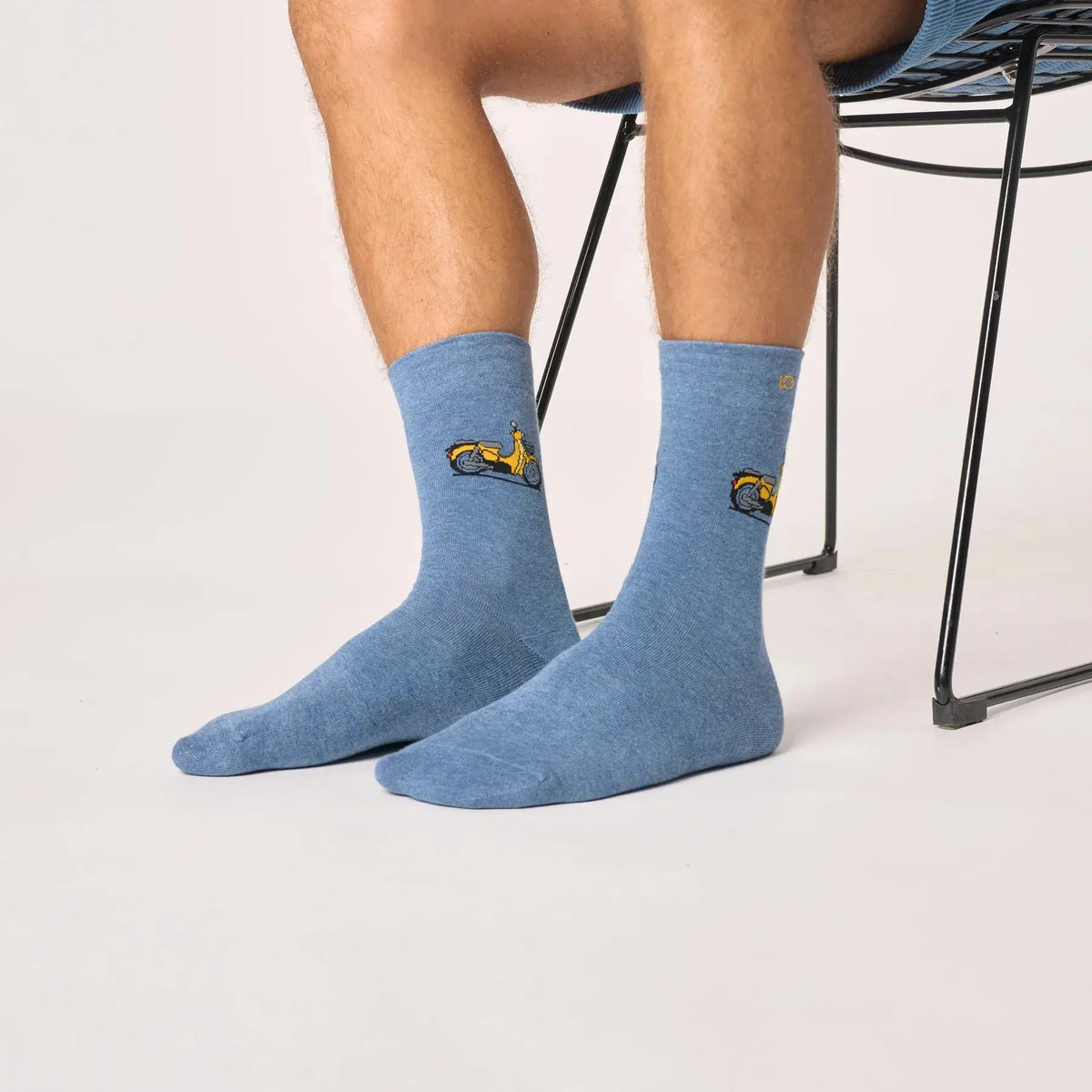 Paire bleu jean chinée portée, scooter jaune visible sur les deux tiges, devant un fauteuil en fil noir