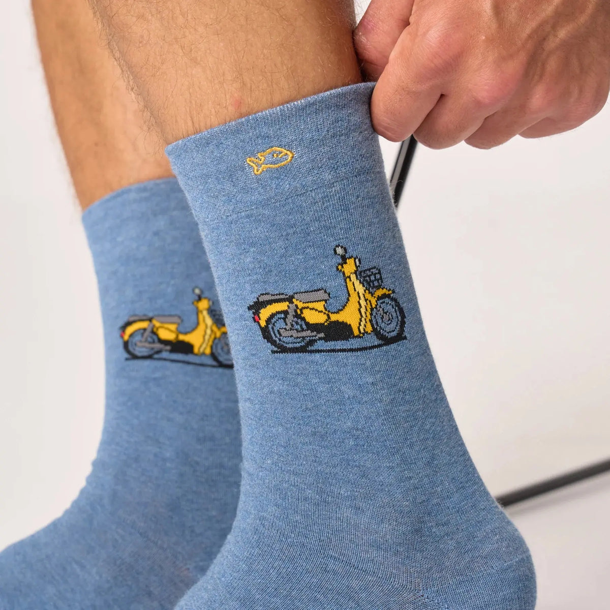 Gros plan sur le scooter jaune au porte-bagages gris, poisson jaune brodé et maille bleu jean chinée