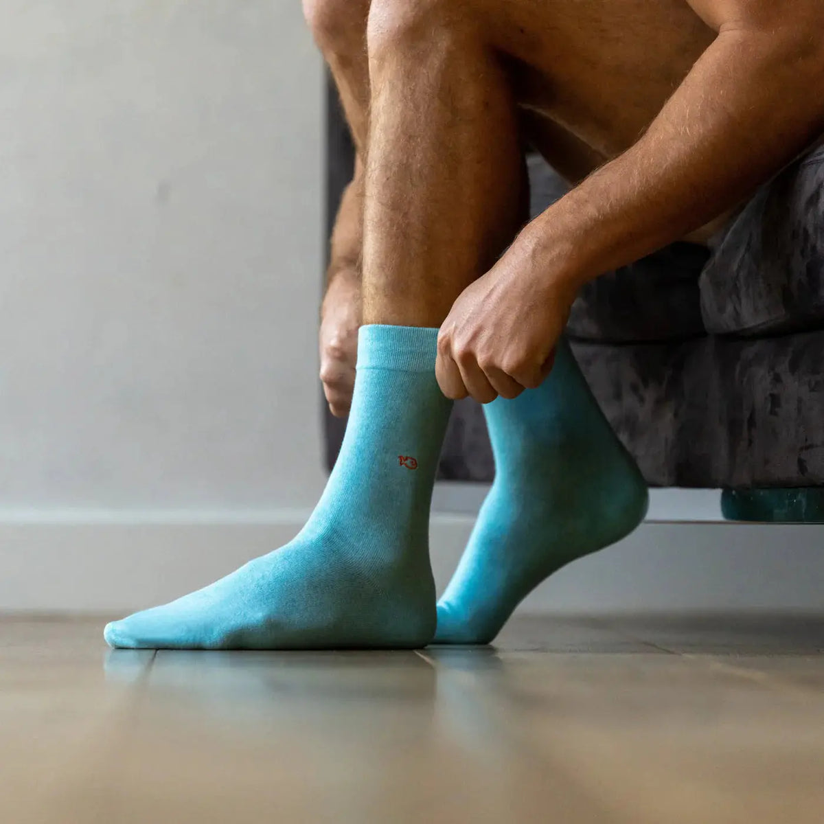 Paire turquoise portée debout, maille unie sans talon ni pointe contrastés, poisson brodé orange visible.