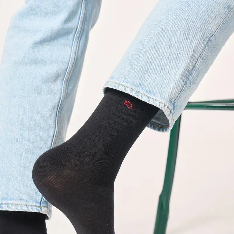 Gros plan sur la tige mi-mollet d'une chaussette noire glissée sous l'ourlet du jean, poisson rouge brodé