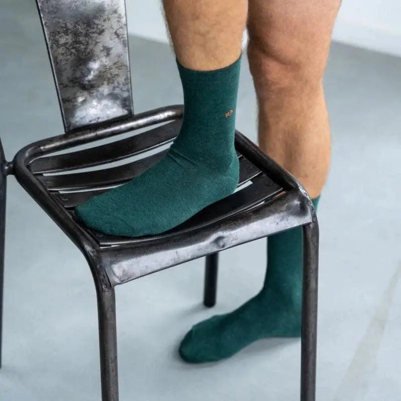Chaussette vert anglais portée, pied posé sur une assise de chaise en métal brut
