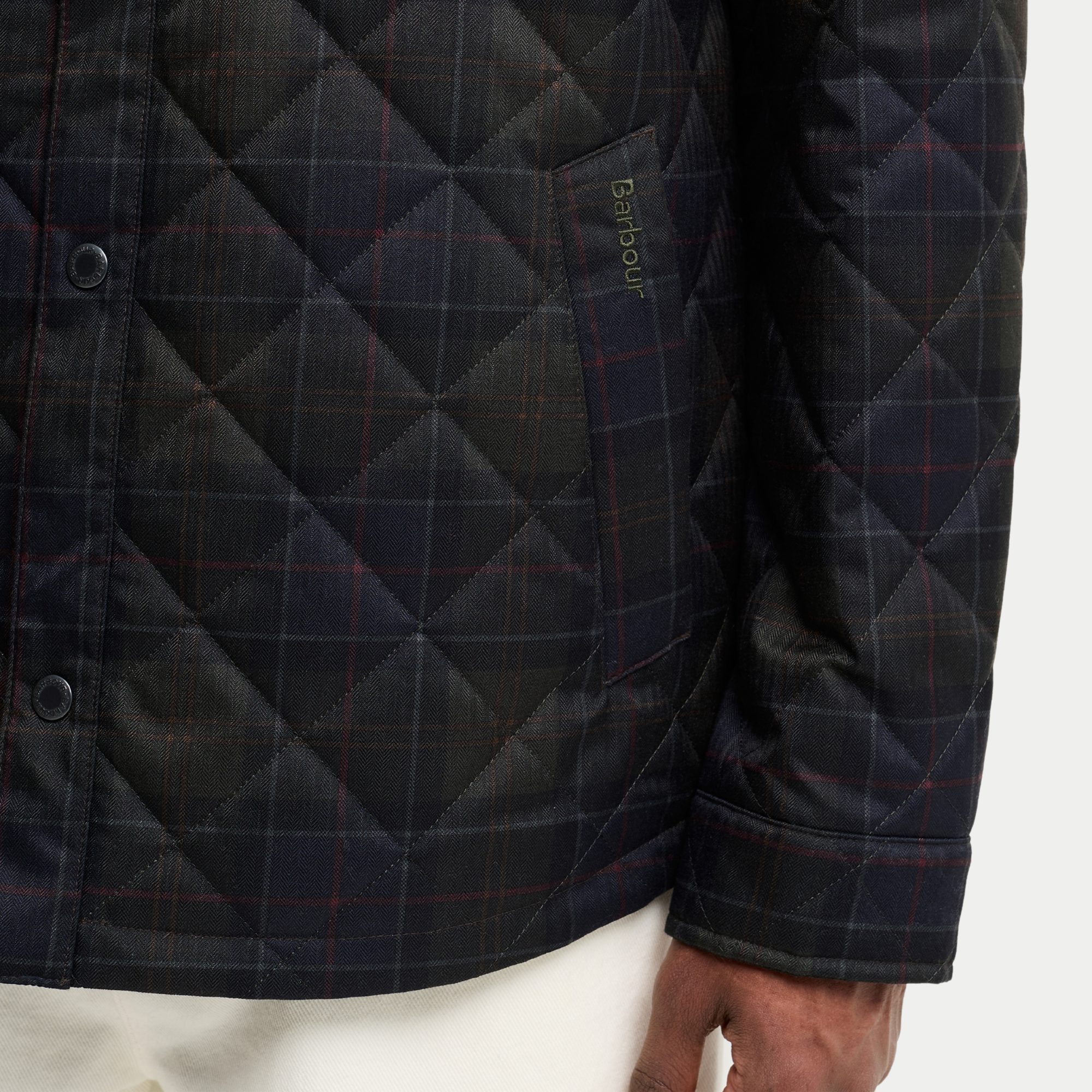 Détail du bas de la veste-chemise matelassée tartan olive foncé : poche basse passepoilée et broderie Barbour vert olive