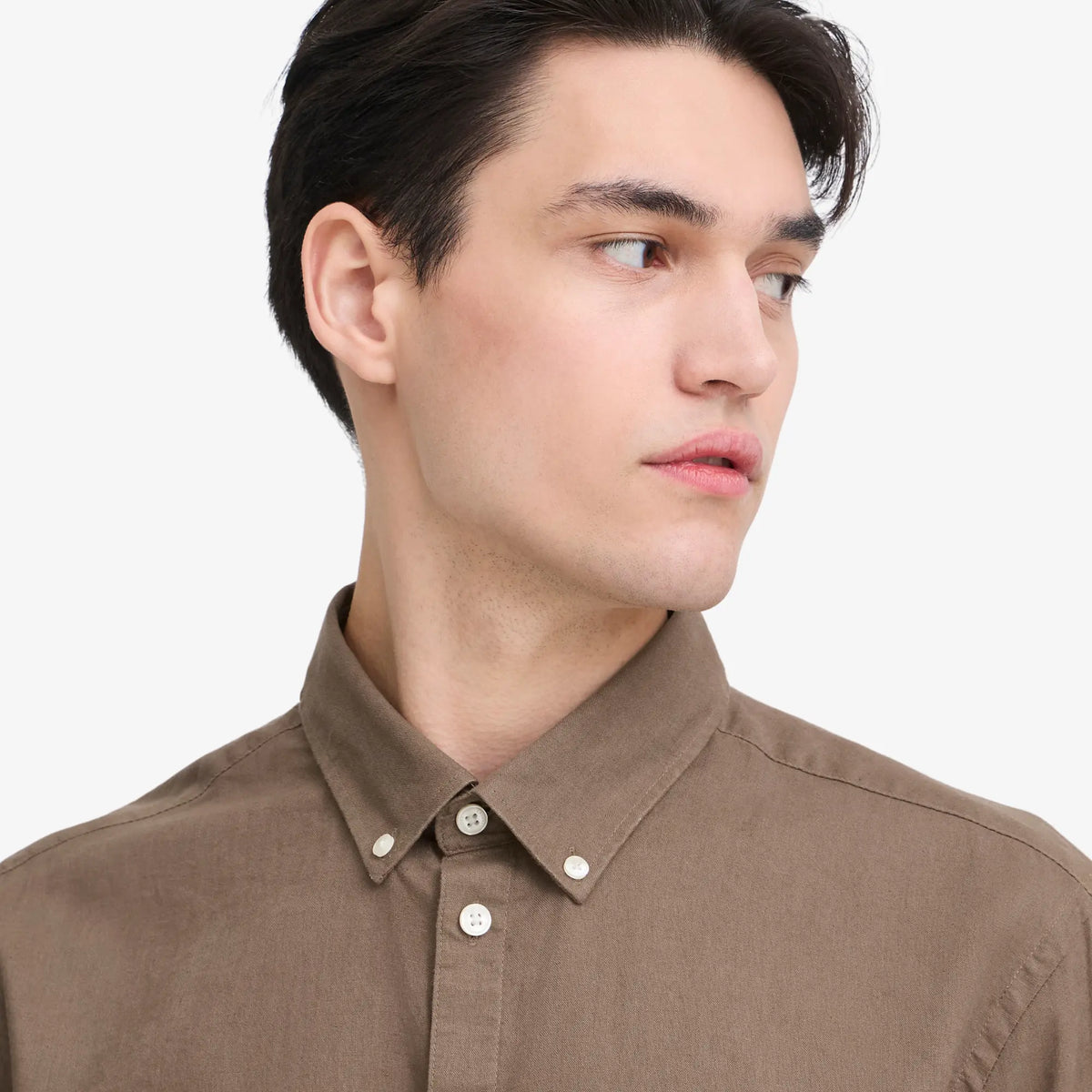Gros plan du col boutonné de la chemise en lin marron et de ses boutons blancs
