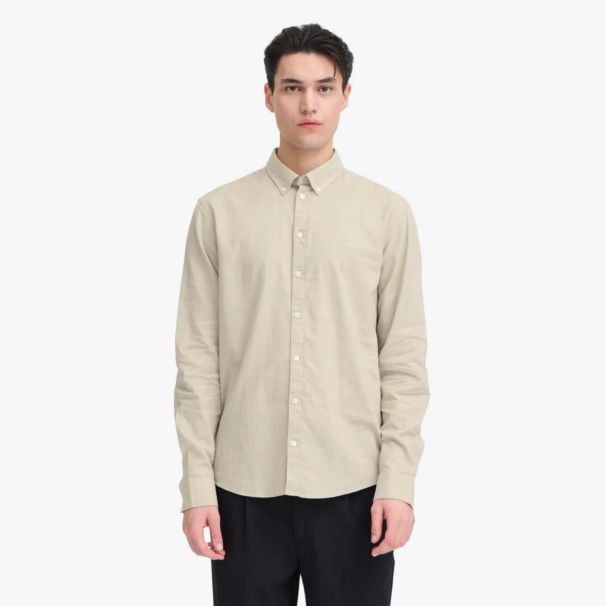 Chemise en lin naturel portée, boutonnée jusqu'en haut sur un pantalon noir