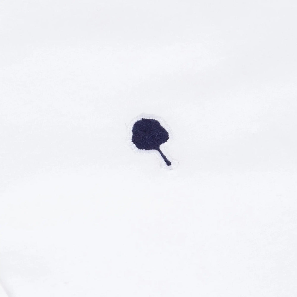 Gros plan de la broderie arbre bleu marine sur le coton écru de la chemise Ivoy
