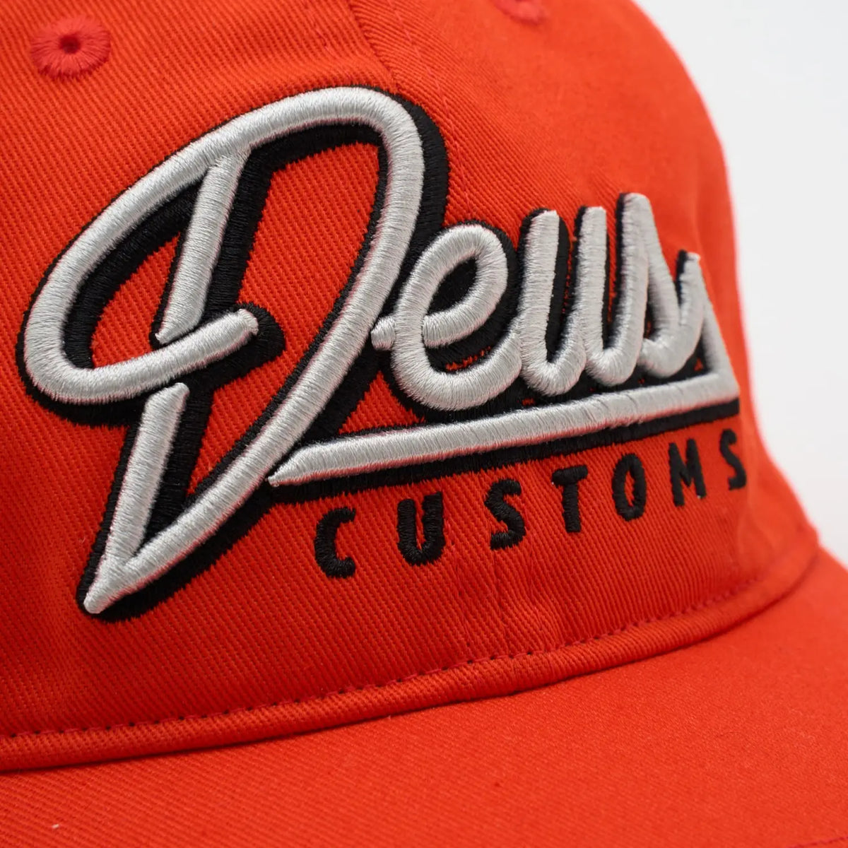 Gros plan du script brodé gris cerné de noir sur la casquette Conduit Cap orange
